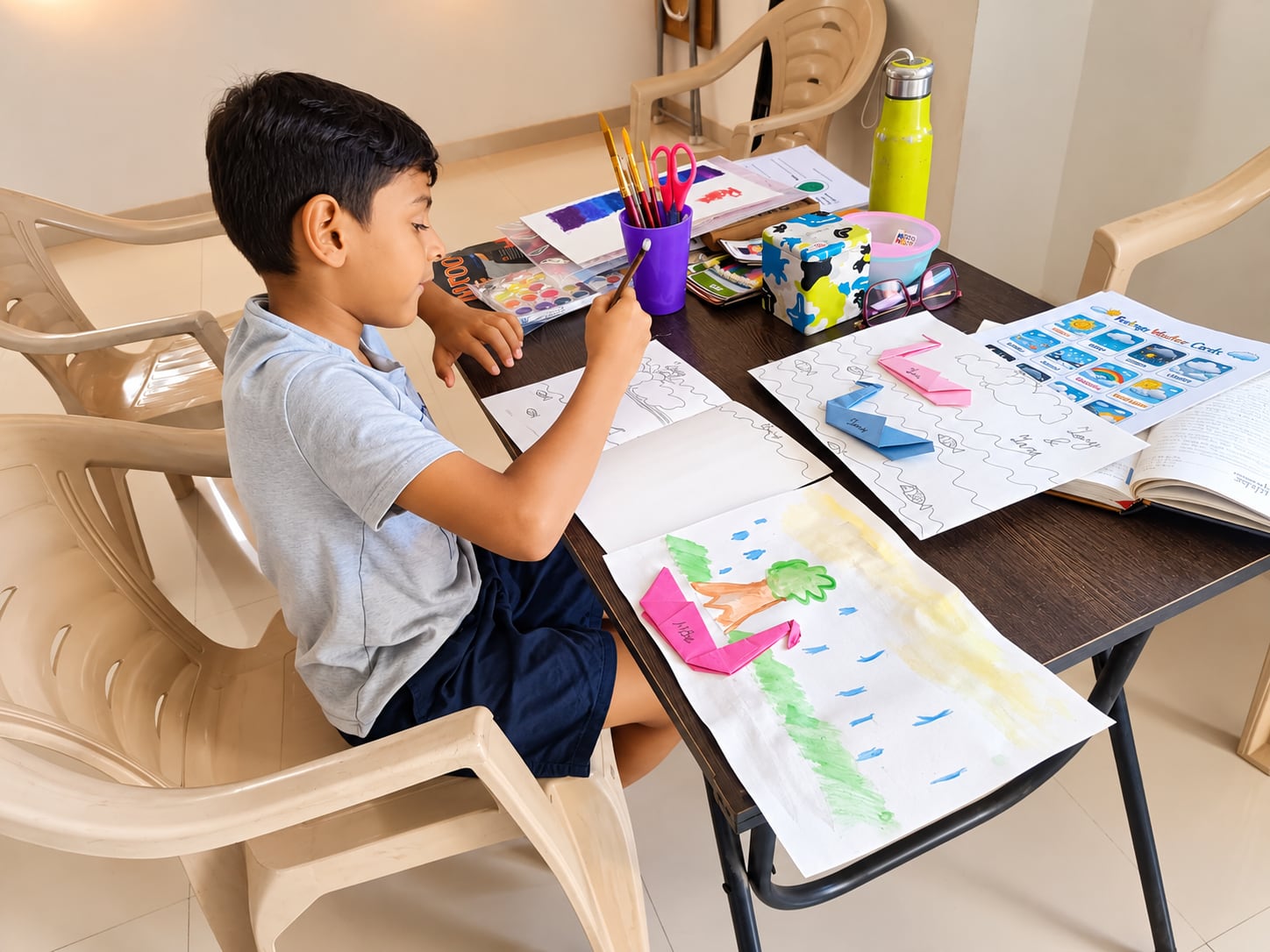 A boy painting at a table during a children’s session at Jatan, with feelings cards beside him